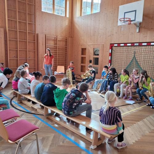 Kinder sitzen im Turnsaal und hören den Musikerinnen zu